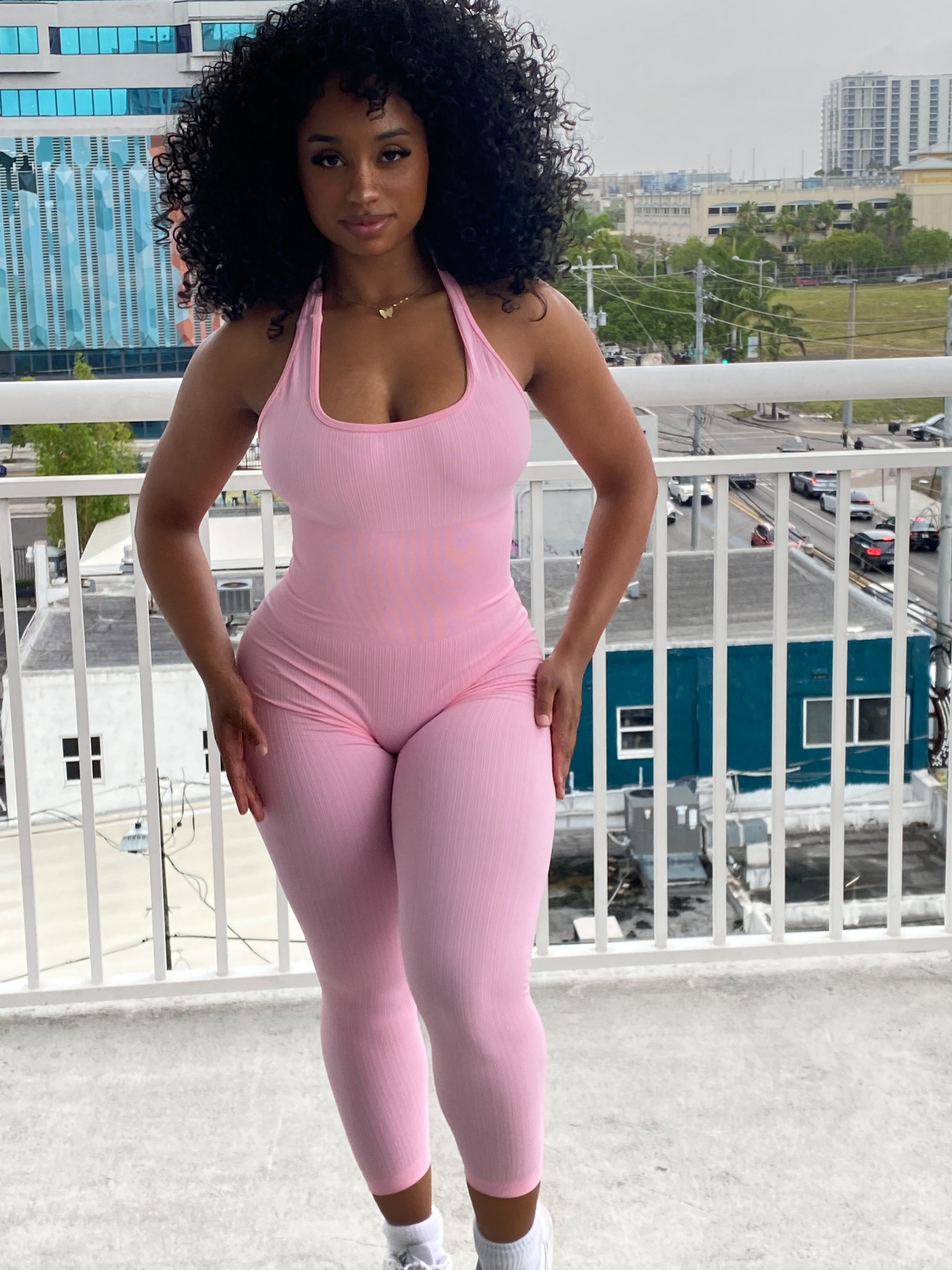 Woman wearing a fitted light pink halter jumpsuit with ribbed fabric, ankle-length leggings, and a scoop neckline.