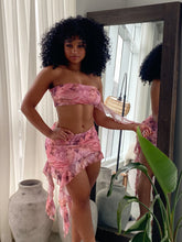 Woman wearing a pink mesh two-piece outfit featuring a strapless bandeau top and ruffled asymmetrical mini skirt with Renaissance-inspired print.