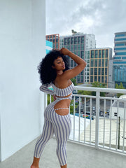 Woman wearing a fitted one-sleeve striped cutout jumpsuit featuring diagonal and hip cutouts, with a cropped ankle-length fit.