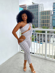 Woman wearing a fitted one-sleeve striped cutout jumpsuit featuring diagonal and hip cutouts, with a cropped ankle-length fit.