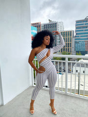 Woman wearing a fitted one-sleeve striped cutout jumpsuit featuring diagonal and hip cutouts, with a cropped ankle-length fit.