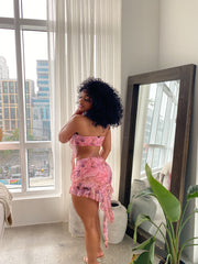 Woman wearing a pink mesh two-piece outfit featuring a strapless bandeau top and ruffled asymmetrical mini skirt with Renaissance-inspired print.