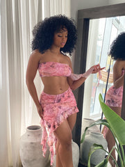 Woman wearing a pink mesh two-piece outfit featuring a strapless bandeau top and ruffled asymmetrical mini skirt with Renaissance-inspired print.