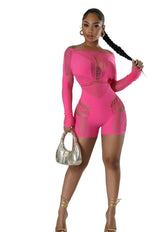 Woman wearing a hot pink mesh cutout romper with long sleeves and off-the-shoulder neckline, featuring intricate knit patterns and body-hugging fit, accessorized with gold heels and a metallic handbag.