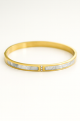 Gold bracelet with a white stone inlay on a white background
