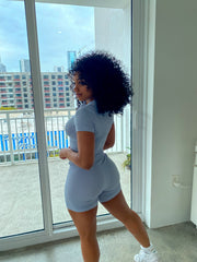 Woman wearing a baby blue ribbed two-piece set with a short-sleeve zip-up crop top and matching high-waisted biker shorts.