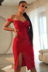 Woman in a red off-shoulder dress standing in a room with a couch and curtains.