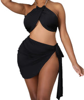 Woman wearing a black two-piece swimwear set featuring a twisted halter bikini top with chain straps and a high-slit side-tie mini sarong-style swim skirt.