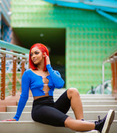 Woman wearing a long sleeve ribbed knit crop top with rhinestone safety-pin closures down the front, paired with high-rise skinny blue jeans.