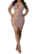 Woman wearing a multicolor sleeveless bodycon mini dress with circular cutouts along the front, secured by small ring details, in a rainbow knit pattern.