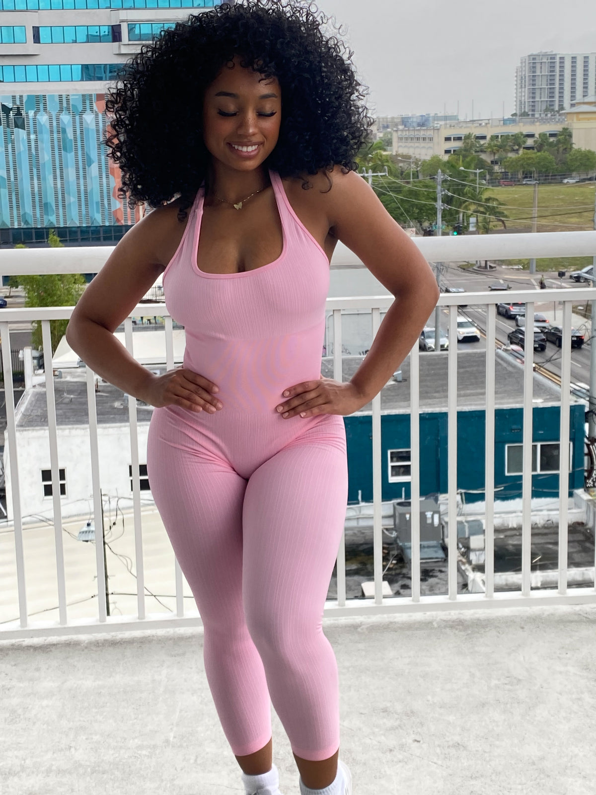 Woman wearing a fitted light pink halter jumpsuit with ribbed fabric, ankle-length leggings, and a scoop neckline.