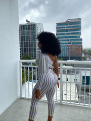 Woman wearing a fitted one-sleeve striped cutout jumpsuit featuring diagonal and hip cutouts, with a cropped ankle-length fit.