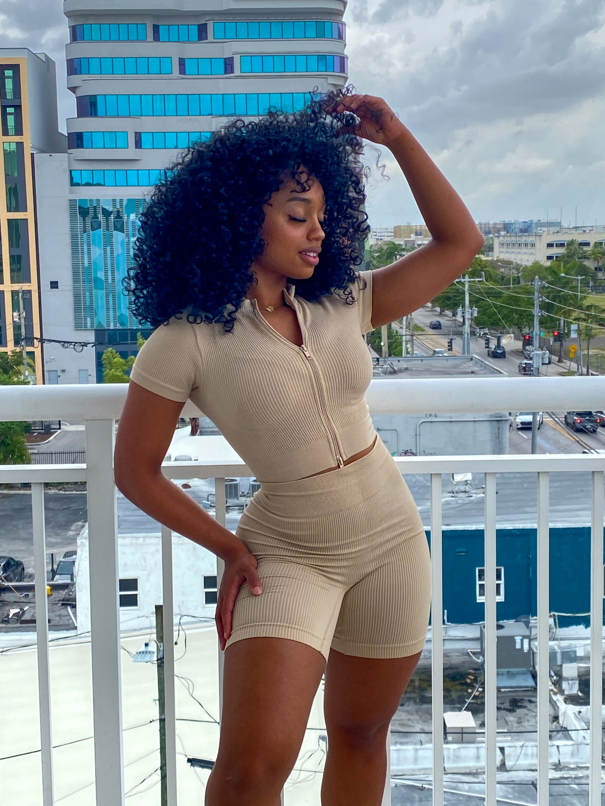 Woman in a beige ribbed two-piece set featuring a zip-up short-sleeve crop top and high-waisted biker shorts.