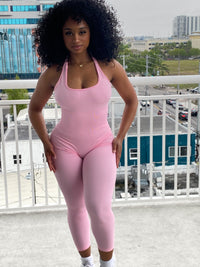 Woman wearing a fitted light pink halter jumpsuit with ribbed fabric, ankle-length leggings, and a scoop neckline.