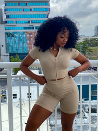 Woman in a beige ribbed two-piece set featuring a zip-up short-sleeve crop top and high-waisted biker shorts.