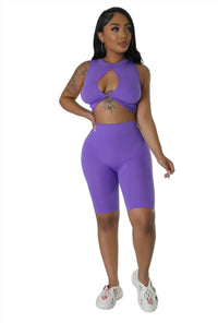 Woman modeling a purple twist-front crop top and matching high-waisted biker shorts with ribbed texture.