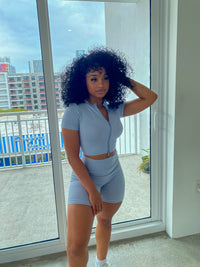 Woman wearing a baby blue ribbed two-piece set with a short-sleeve zip-up crop top and matching high-waisted biker shorts.