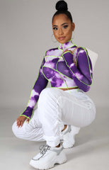 Woman wearing a long sleeve purple and white tie-dye mock neck crop top with neon green contrast stitching.