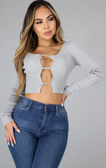 Woman wearing a long sleeve ribbed knit crop top with rhinestone safety-pin closures down the front, paired with high-rise skinny blue jeans.