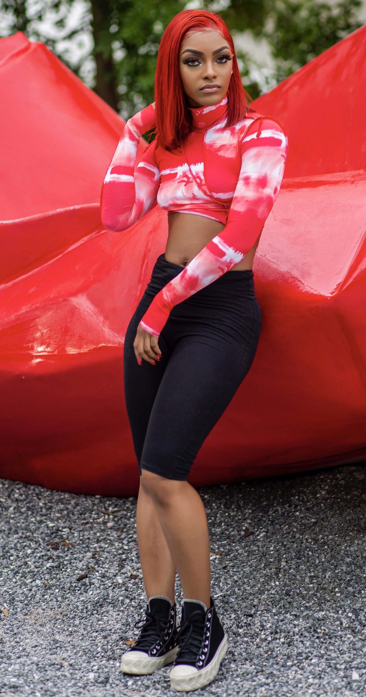 Woman modeling a red and white tie-dye mock neck crop top with contrast seam detail and thumbhole sleeves.