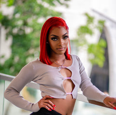 Woman wearing a long sleeve ribbed knit crop top with rhinestone safety-pin closures down the front, paired with high-rise skinny blue jeans.