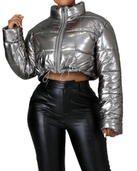Woman wearing a metallic silver cropped puffer jacket with front zipper closure and drawstring hem, paired with high-waisted black faux leather pants.
