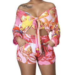 Woman wearing a colorful long-sleeve tie-front crop top and matching printed high-waist shorts with a bold baroque and chain pattern.